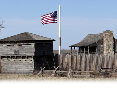 A wooden fort with one large watch tower and one residential building surrounded by a fence. Inside the fort, an American Flag flies high above the building.