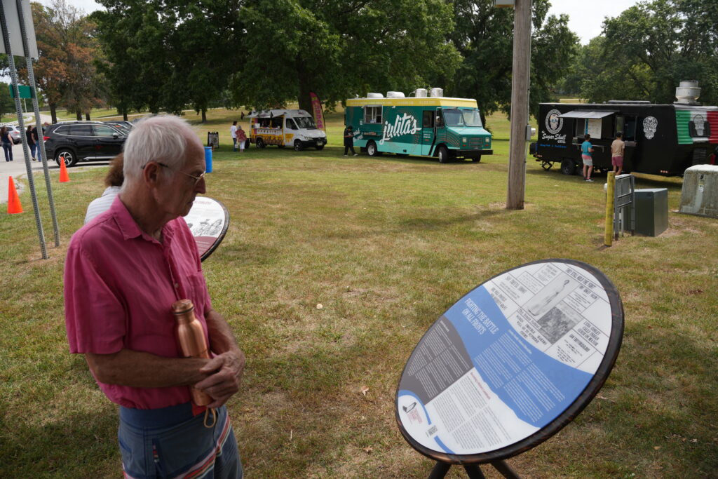 A man reads a panel at the Fort Conley exhibit. The panel is on a circular wooden frame and shows the history of the Wyandot people.