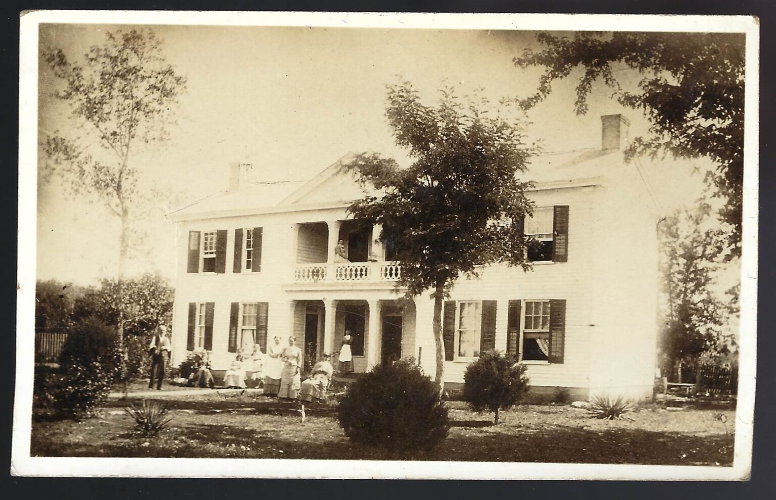 19th Century photo of the Majors House. The white two-story structure has an open portico and a group of people sitting on the front law.