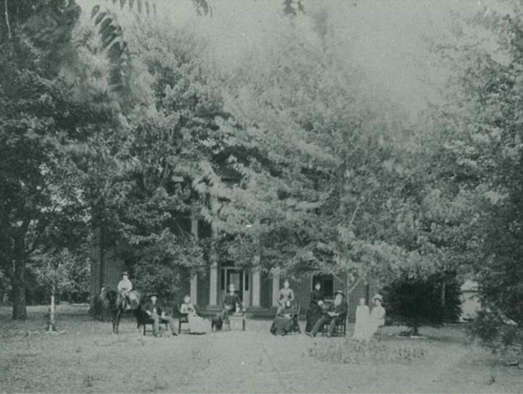 The Wornall House in the 1890s. Much of the structure is obscured by trees, but the Wornall family is seated out front.
