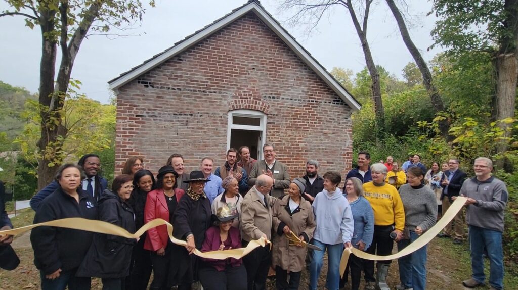 Group of people cut a ribbon in front of a brick building.