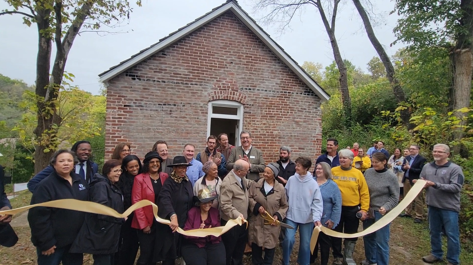 Group of people cut a ribbon in front of a brick building.