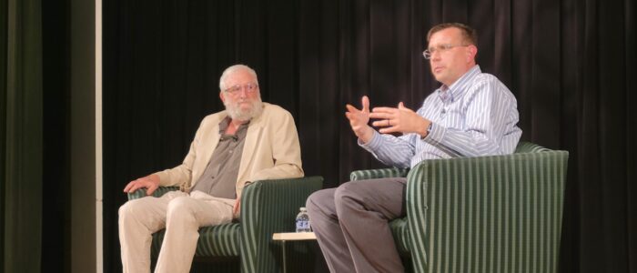 Two men sit on stage