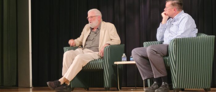 Two men sit on stage