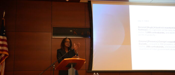 Woman stands at podium with presentation behind her